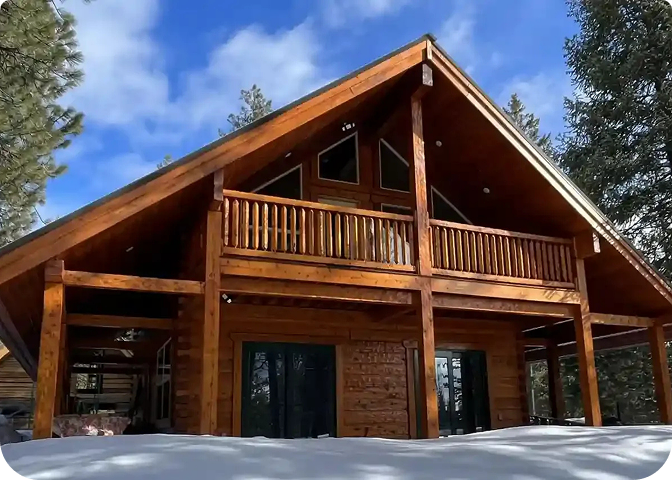 A stunning log cabin made of rich red cedar nestled among tall pinasde trees under a clear blue sky.