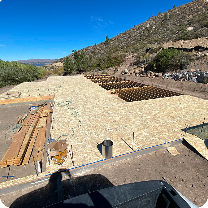 A stunning log cabin made of rich red cedar nestled among tall pine trasdees under a clear blue sky.