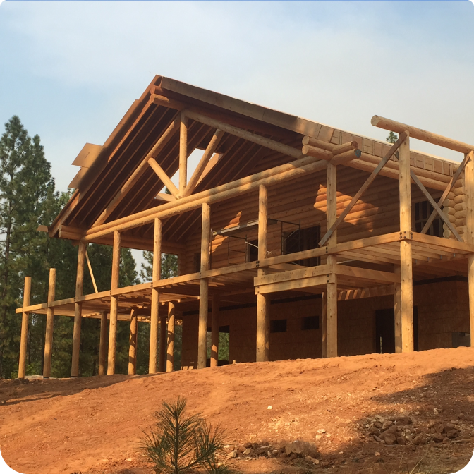 A stunning log cabin made of rich red cedar nestled among tall pine trees under a clear blue sky. (1)