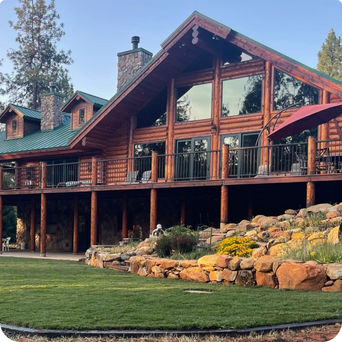 A stunning log cabin made of rich red cedar nestled among tall pine trees under a clear blue sky. (2)