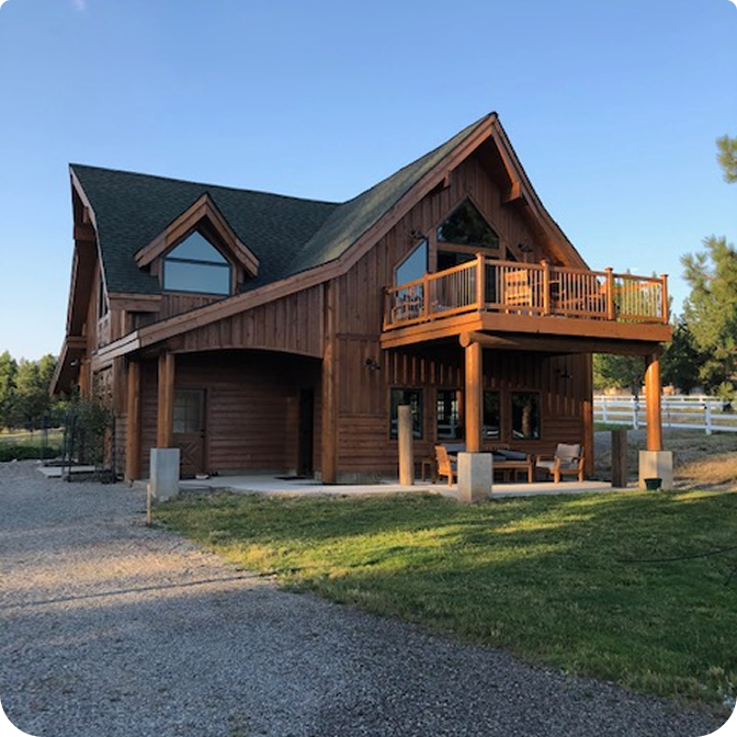 A stunning log cabin made of rich red cedar nestled among tall pine trees under ayu clear blue sky.