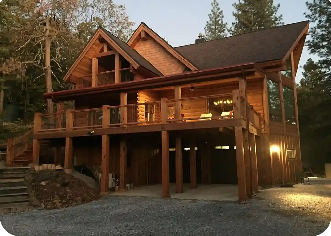 A stunning log cabin made of rich red cedar nestled among tall pine trfjees under a clear blue sky.