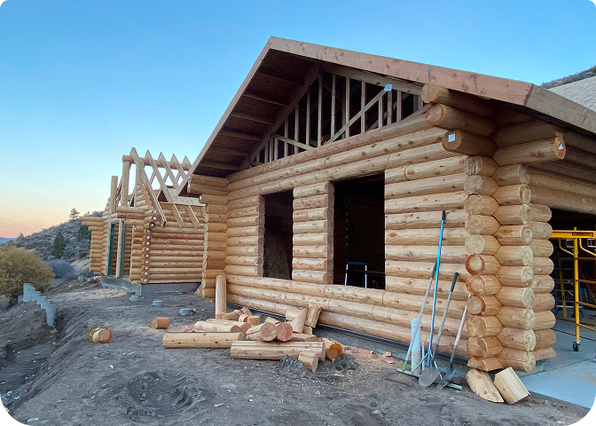 A stunning log cabin made of rich red cedar nestledqw among tall pine trees under a clear blue sky.